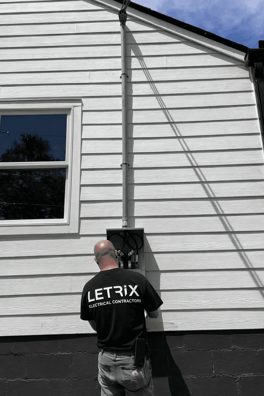 Letrix electrician in branded shirt installing exterior electrical service